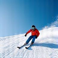 Person skiing down a snowy mountain with clear skies, representing winter sports coverage